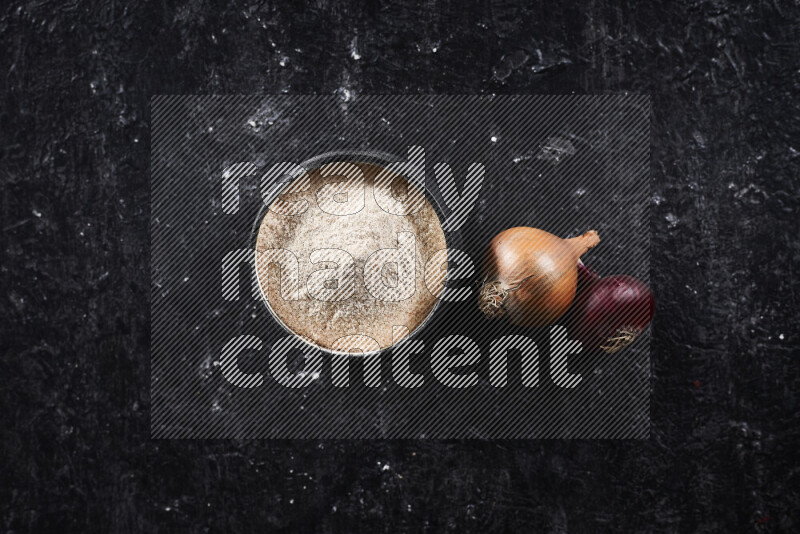 A black pottery bowl full of onion powder on black background