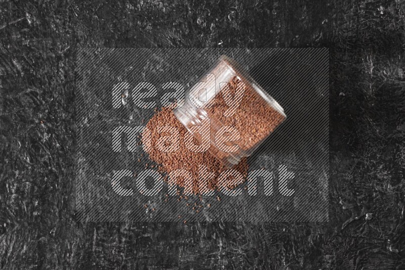 وعاء زجاجي مقلوب ممتلئ ببذور حب الرشاد وتناثرت البذور منه على أرضية سوداء