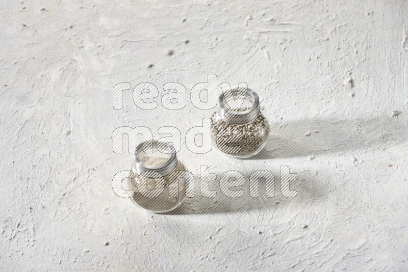 2 Herbal Glass jar full of white pepper beads and powder on textured white flooring