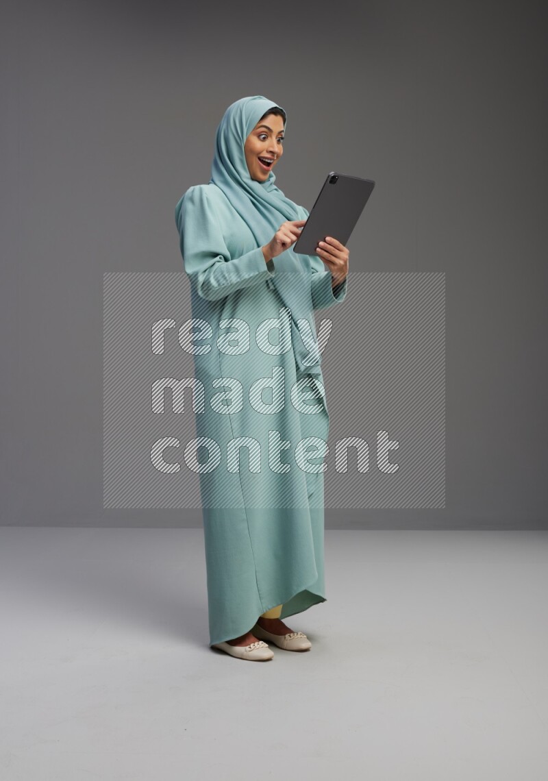 Saudi Woman wearing Abaya standing working on tablet on Gray background