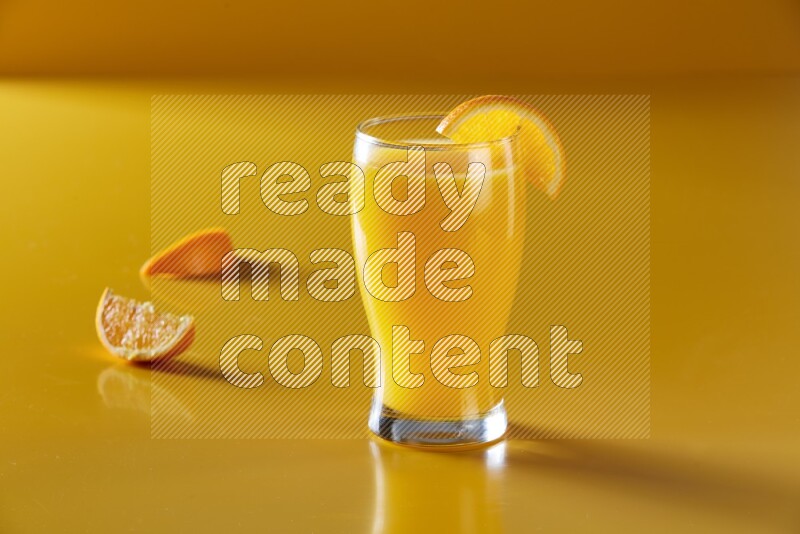 glass of orange juice with orange slice on yellow background