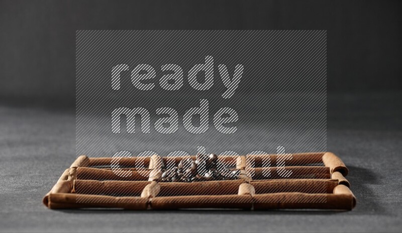 9 squares of cinnamon sticks full of coffee beans in the middle surrounded by nutmeg, dried mint, cloves, dried basil, dried ginger, cinnamon, star anise and cardamom on black flooring