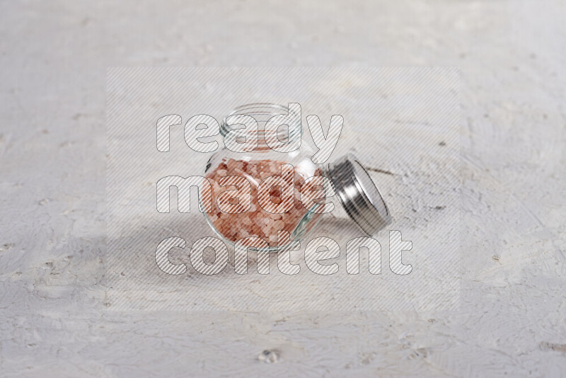 A glass jar full of coarse himalayan salt crystals on white background