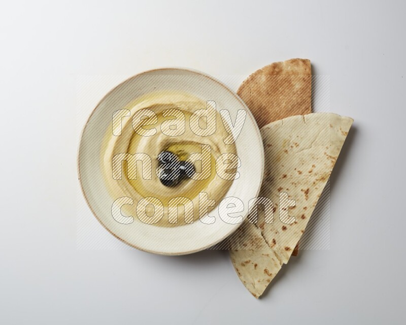 Hummus in a pottry plate garnished with black olives on a white background