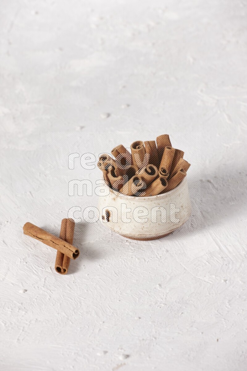 Cinnamon sticks in a beige bowl on a white background