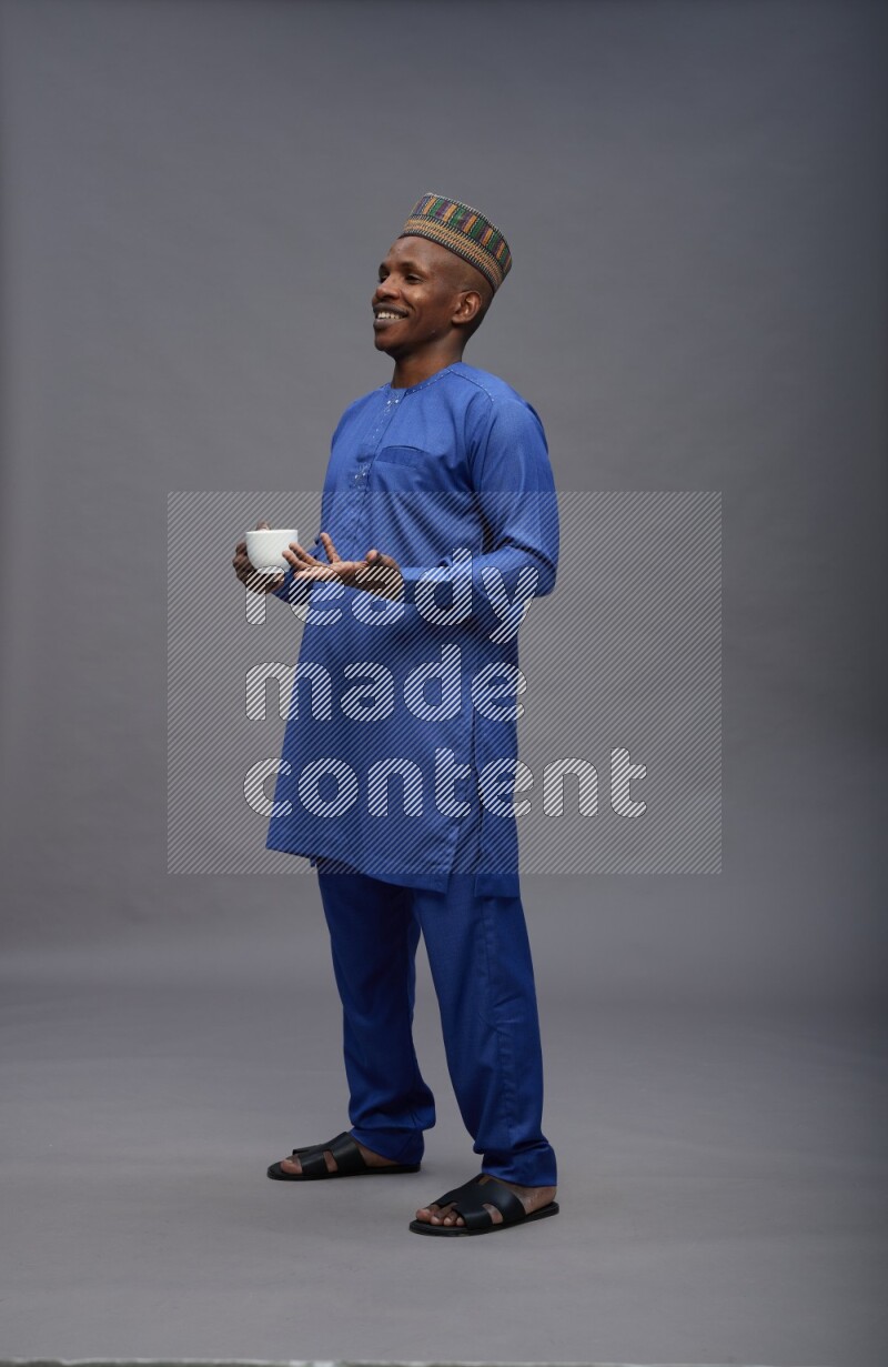 Man wearing Nigerian outfit standing holding mug on gray background