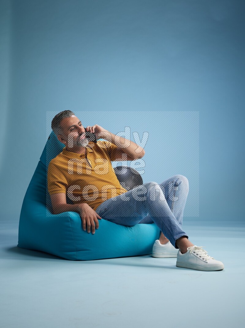 A man sitting on a blue beanbag and talking on the phone