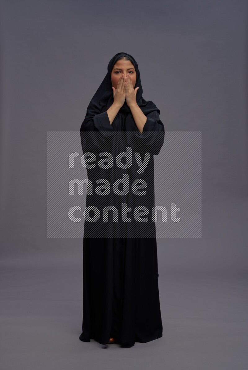 Saudi woman wearing Abaya standing hands behind head on gray background