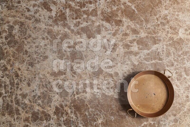 A small copper pan on beige marble background