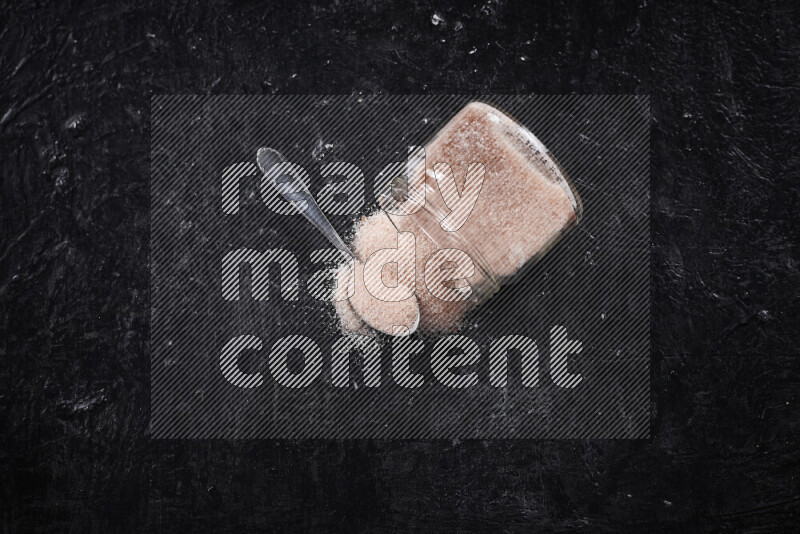 A glass jar full of fine himalayan salt on black background