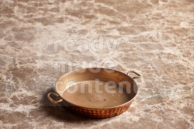 A small copper pan on beige marble background