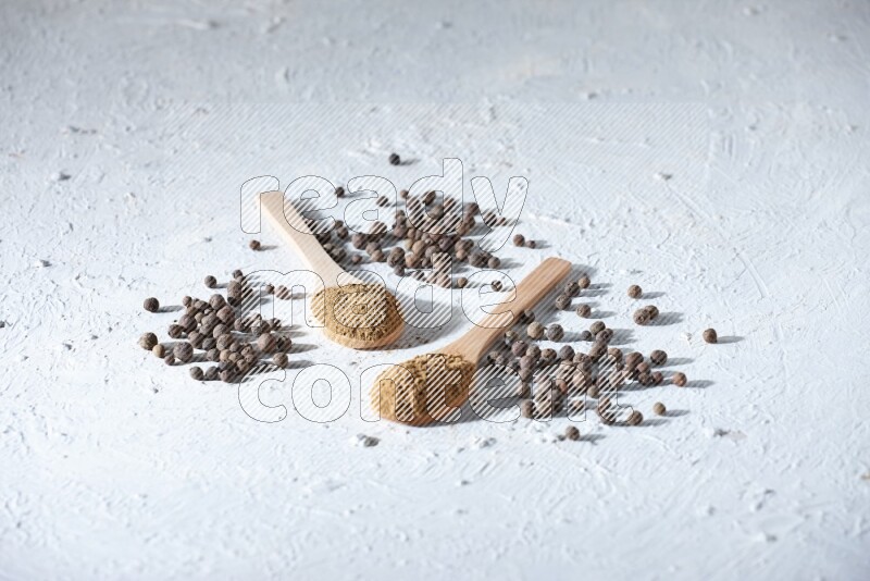 Wooden spoons full of allspice powder and allspice whole balls spreaded on a textured white flooring