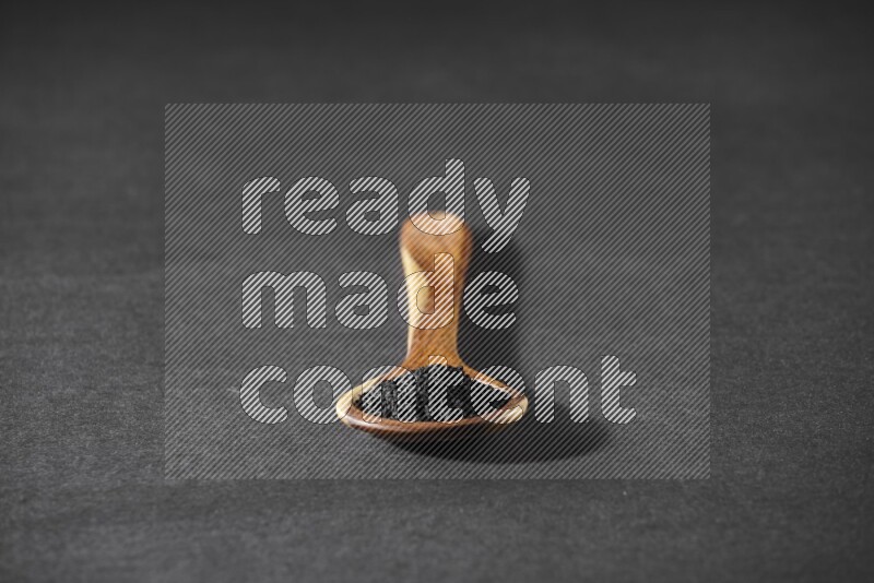 A wooden ladle full of black seeds on a black flooring