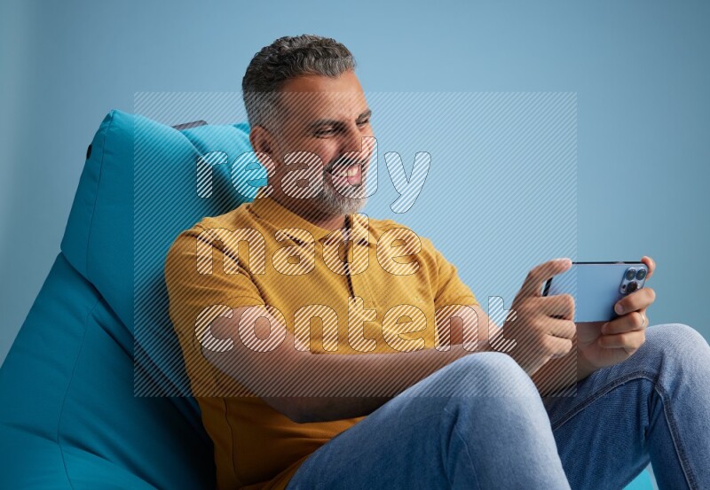 A man sitting on a blue beanbag and playing on phone