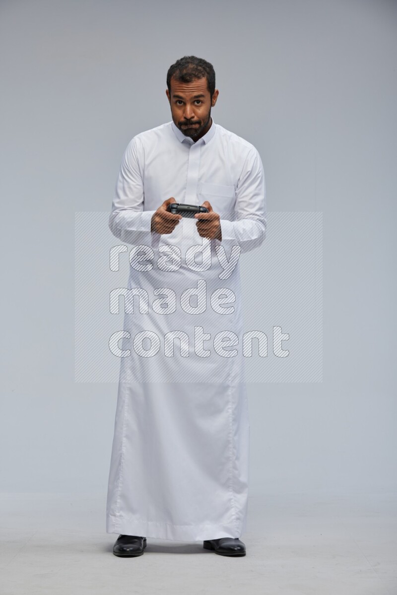 Saudi man Wearing thob standing holding joystick on Gray background
