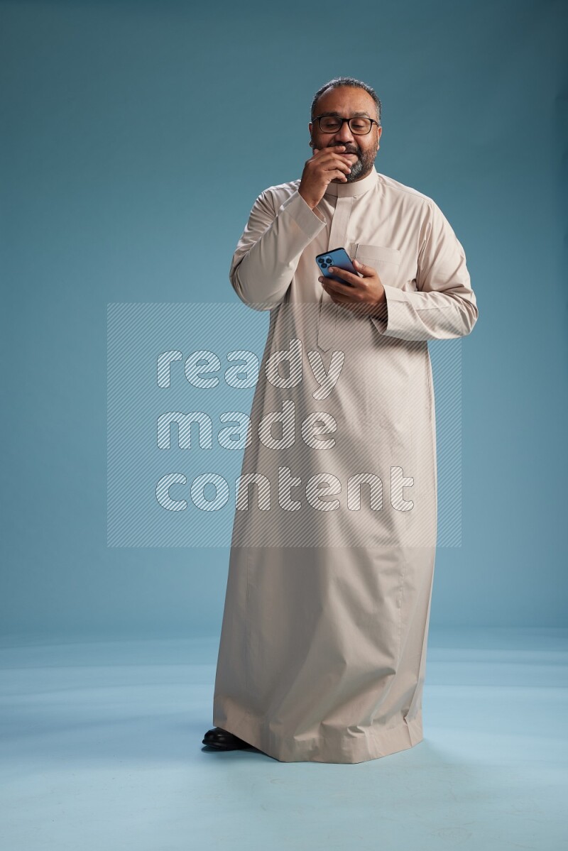 Saudi Man without shimag Standing texting on phone on blue background