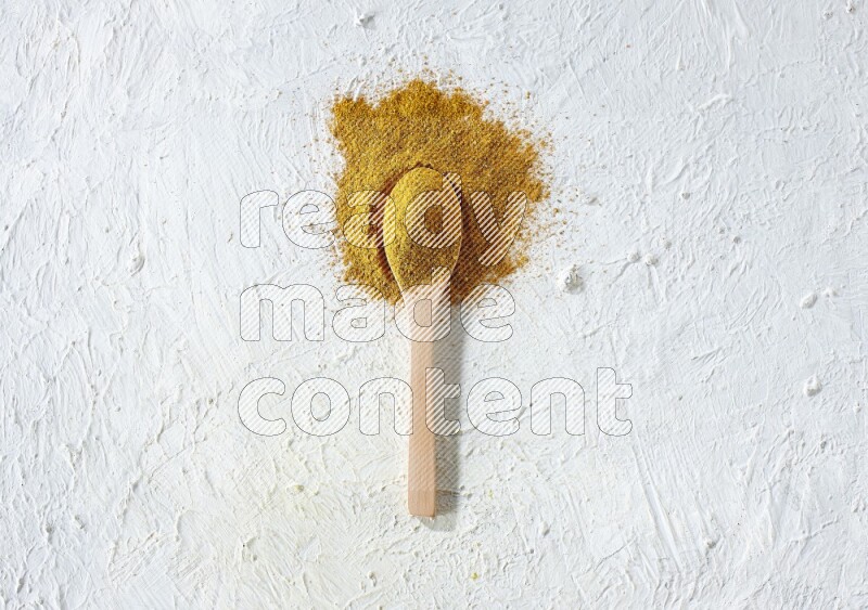 A wooden spoon full of turmeric powder on textured white background