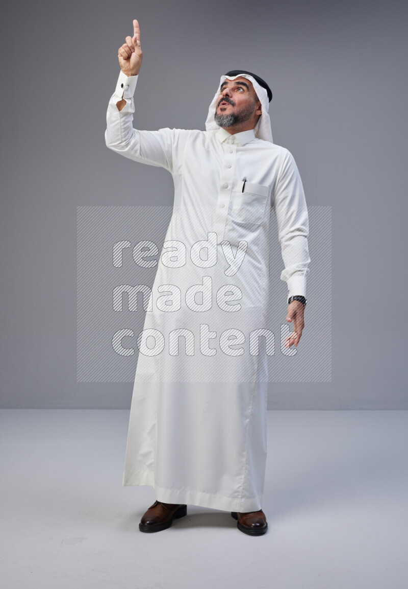 Saudi man Wearing Thob and white Shomag standing interacting with the camera on Gray background