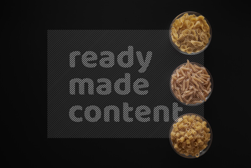 Different pasta types in 3 glass bowls on black background