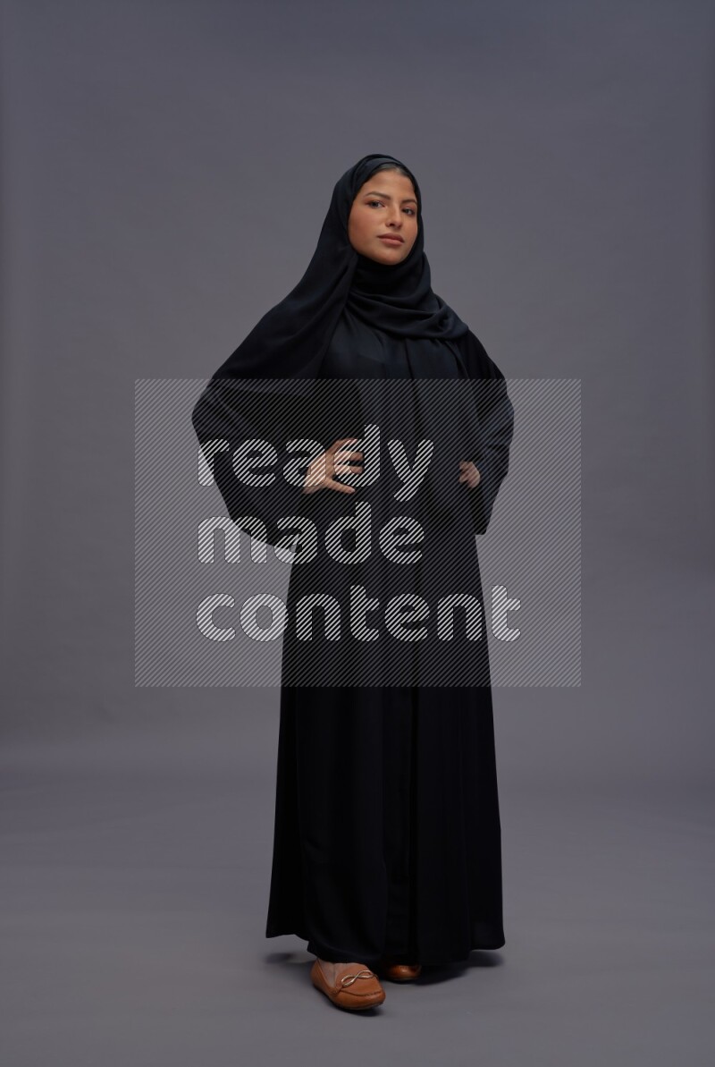 Saudi woman wearing Abaya standing interacting with the camera on gray background