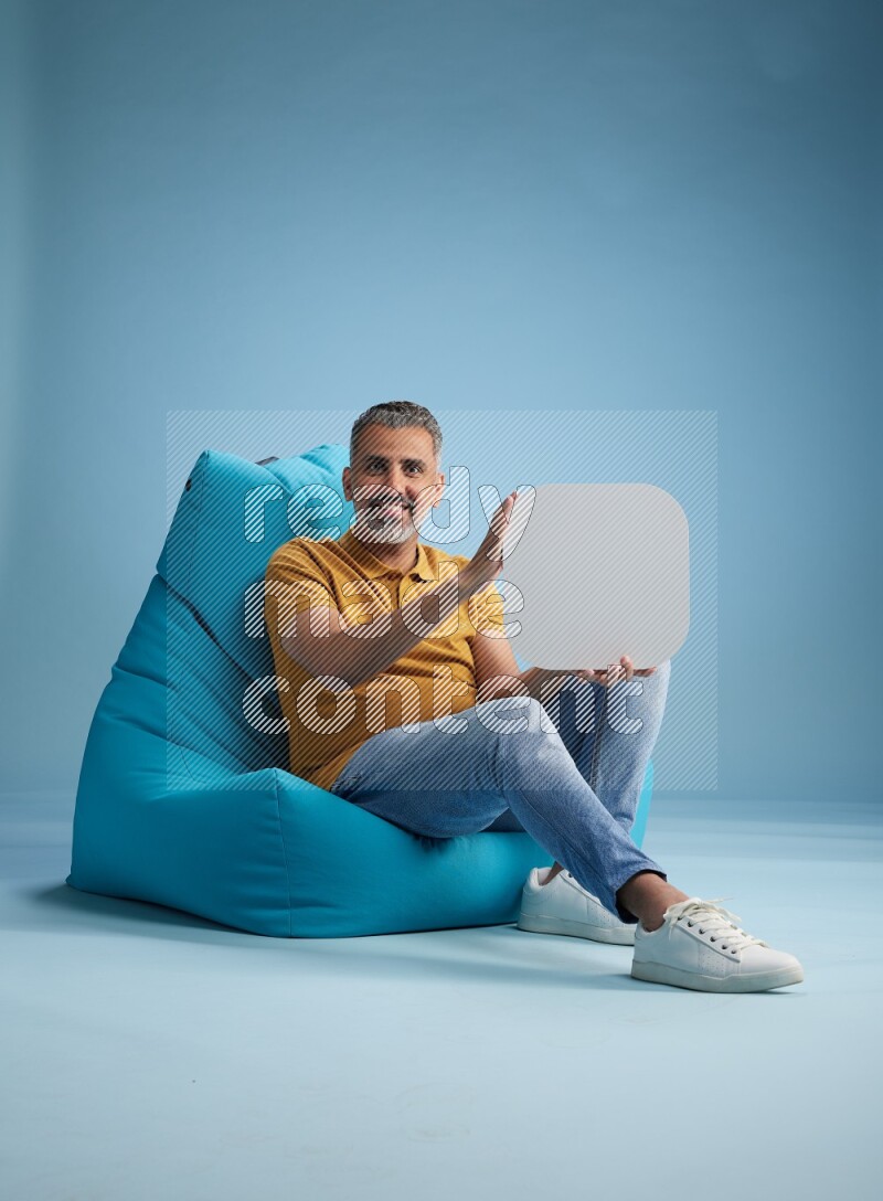 A man sitting on a blue beanbag and holding social media sign