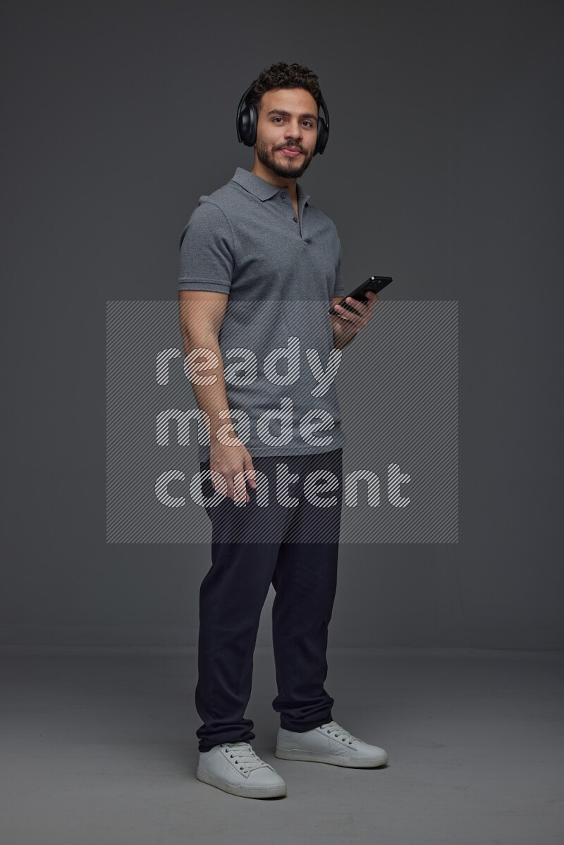 A man wearing casual and using his phone and headphone eye level on a gray background