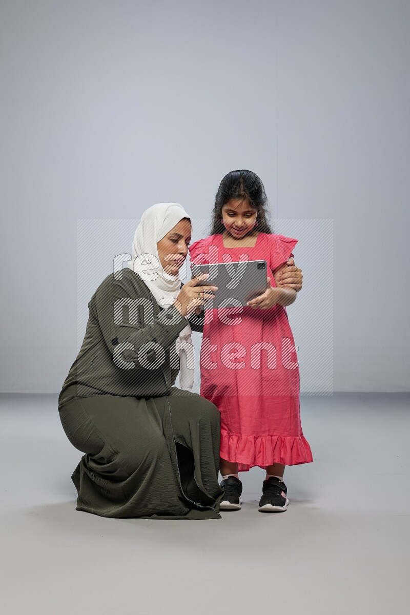 A girl holding an Ipad with her mother on gray background