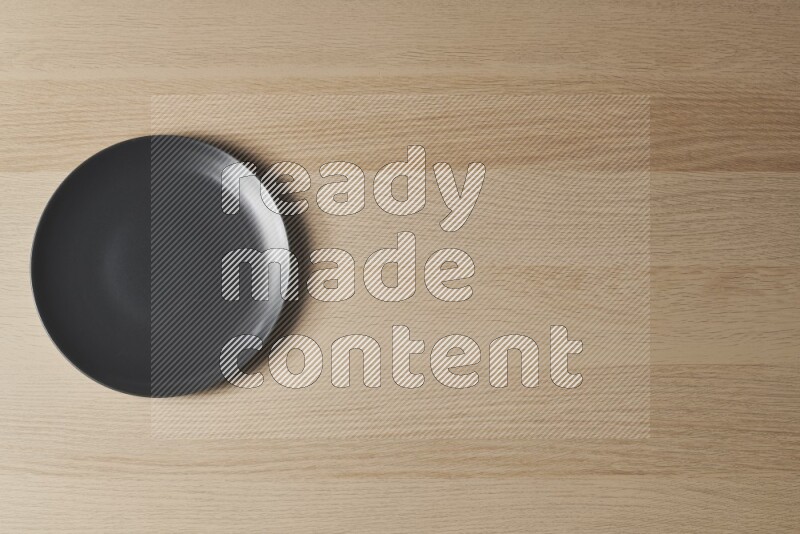A black ceramic circular plate on light wooden background