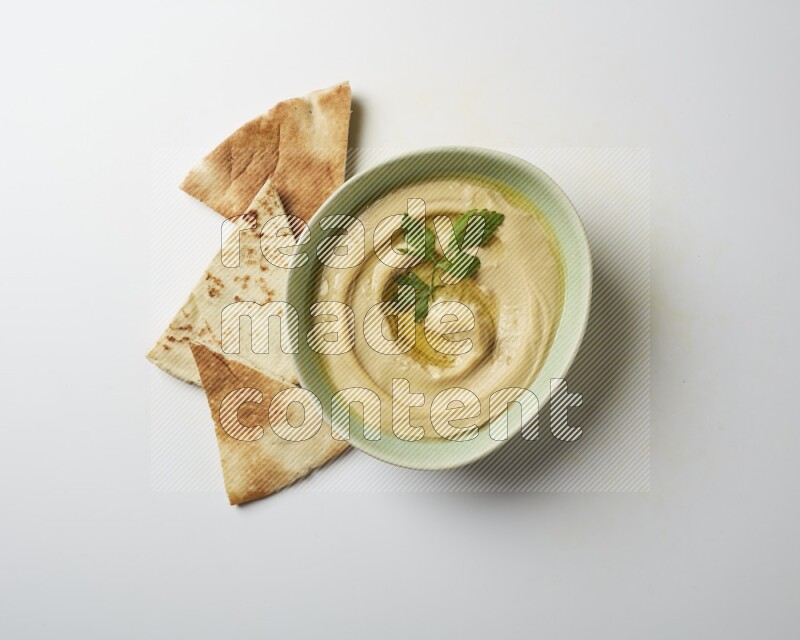 Hummus in a green plate garnished with parsley on a white background