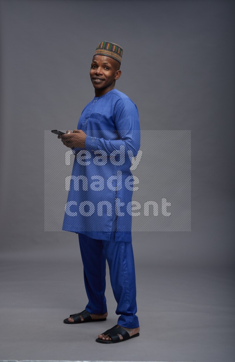 Man wearing Nigerian outfit standing texting on phone on gray background