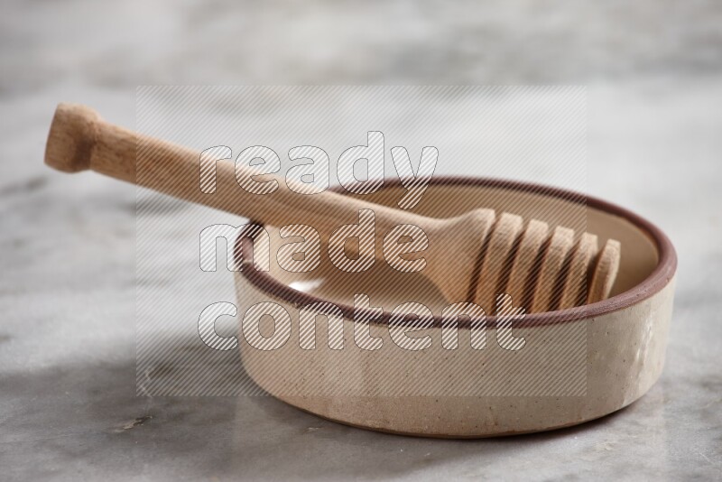 Beige Pottery Oven Bowl with wooden honey handle on the side with grey marble flooring, 15 degree angle
