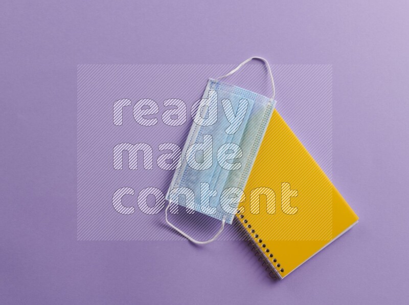 A yellow notebook with school supplies on purple background