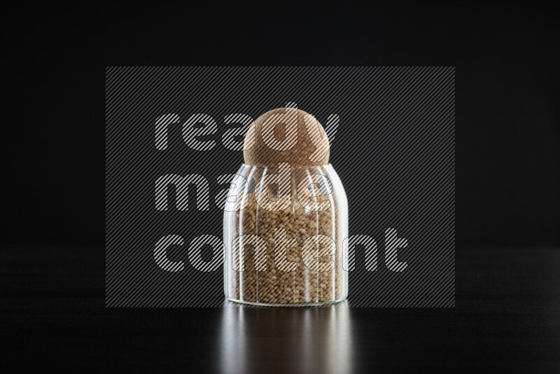 Hulled wheat in a glass jar on black background