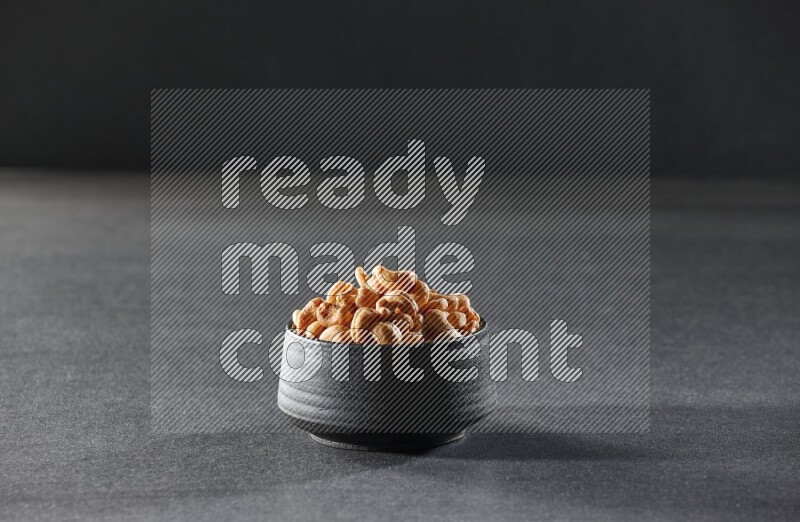 A black pottery bowl full of cashews on a black background in different angles