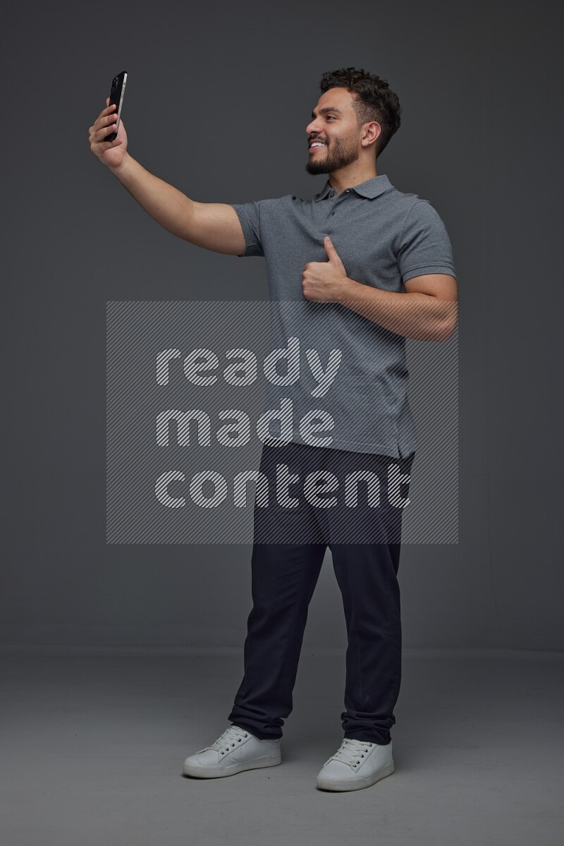 A man wearing casual and taking selfie with his phone different angles eye level on a gray background