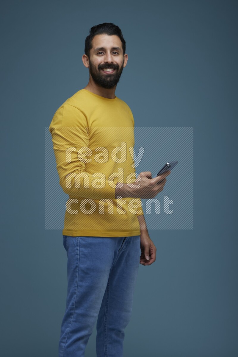 Man posing with a phone in a blue background wearing a yellow shirt