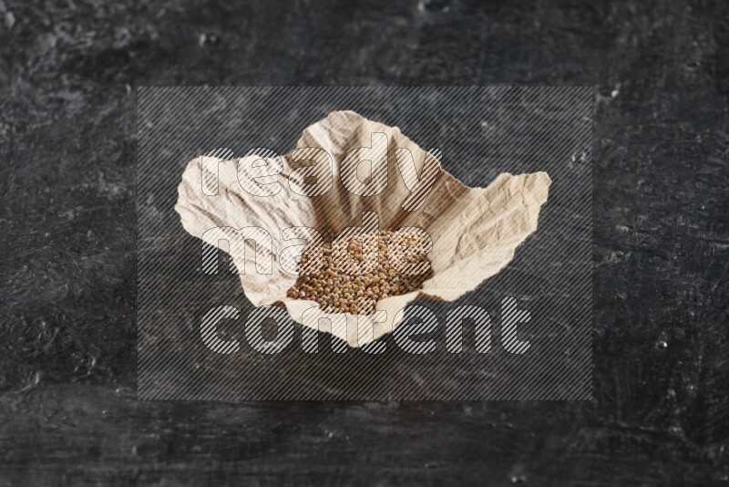 A crumpled piece of paper full of mustard seeds on a textured black flooring