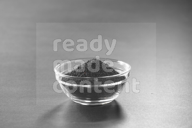 A glass bowl full of black seeds on black flooring