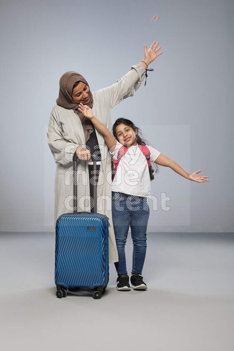 Mom and daughter standing pulling a carry-on bag on gray background