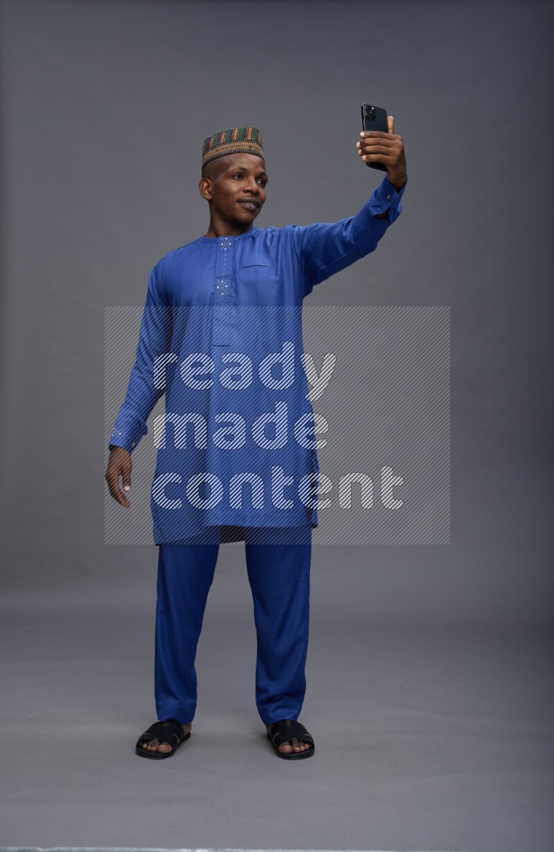 Man wearing Nigerian outfit standing taking selfie on gray background