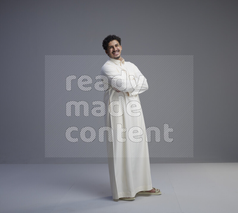 A Saudi man standing wearing thob interacting with the camera on gray background