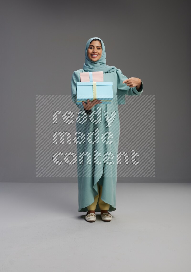 Saudi Woman wearing Abaya standing holding gift box on Gray background