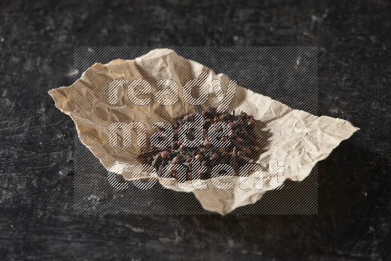 Cloves in crumpled piece of paper on a textured black flooring