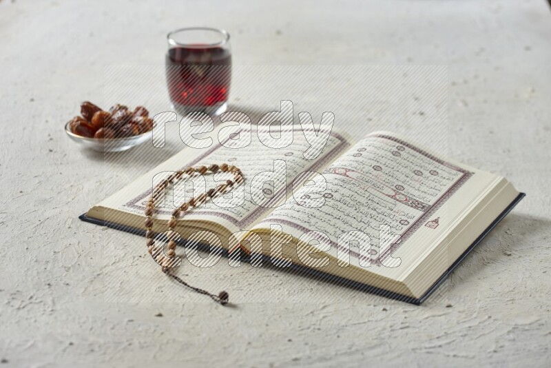 Quran with dates, prayer beads and different drinks all placed on textured white background