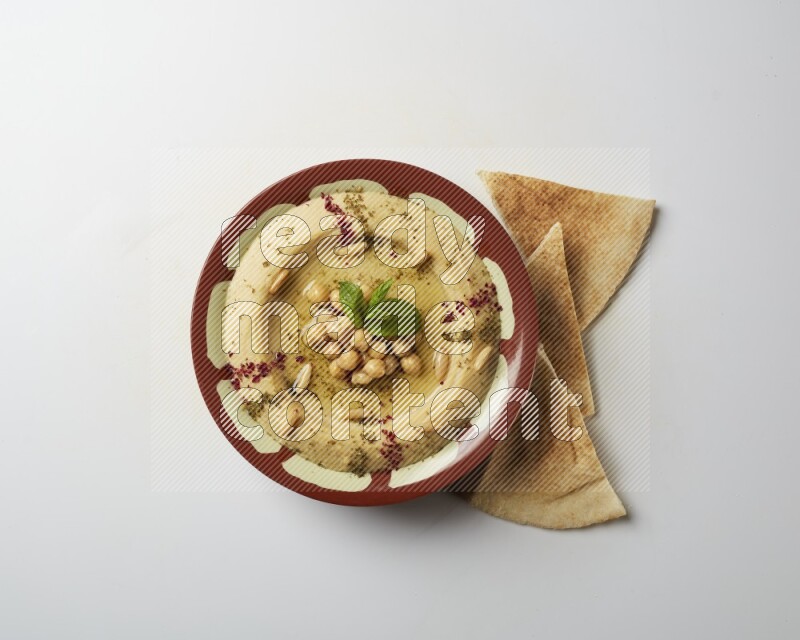 Hummus in a traditional plate garnished with zaatar & sumak on a white background