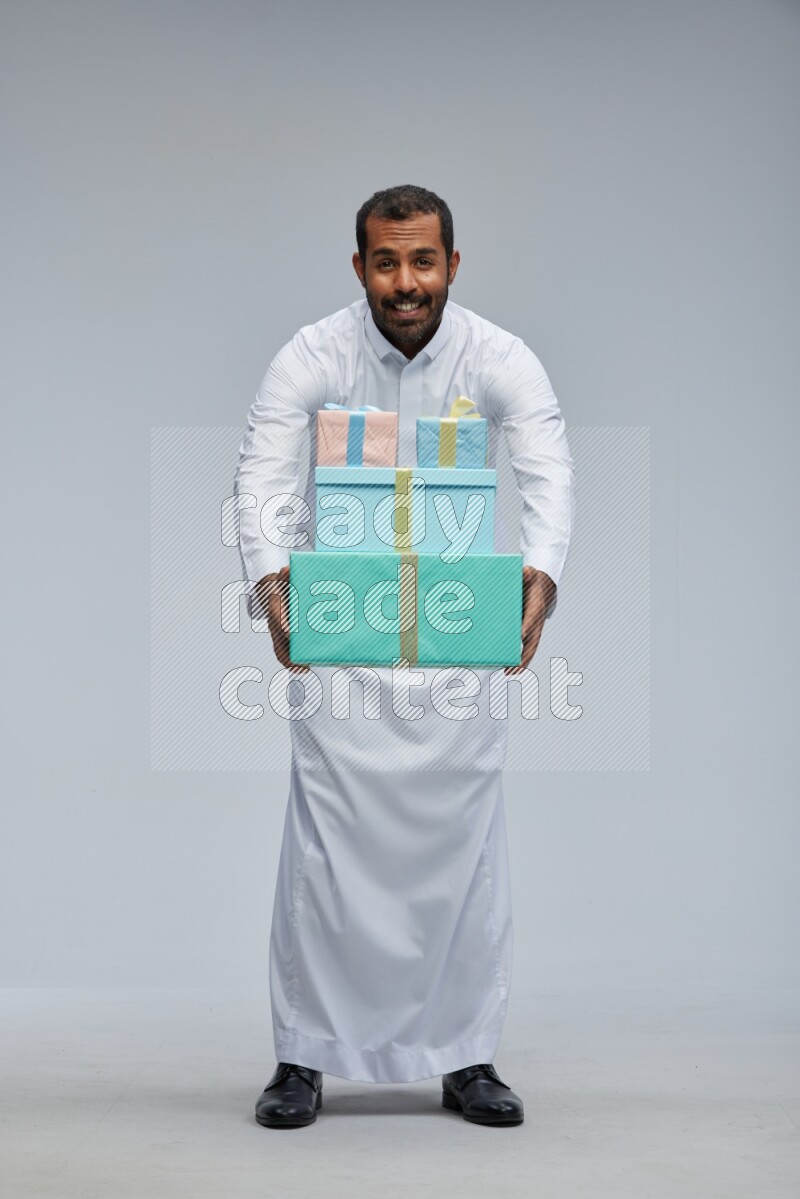 Saudi man Wearing thob standing holding gift box on Gray background