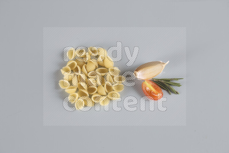 Raw pasta with different ingredients such as cherry tomatoes, garlic, onions, red chilis, black pepper, white pepper, bay laurel leaves, rosemary, cardamom and mushrooms on light blue background