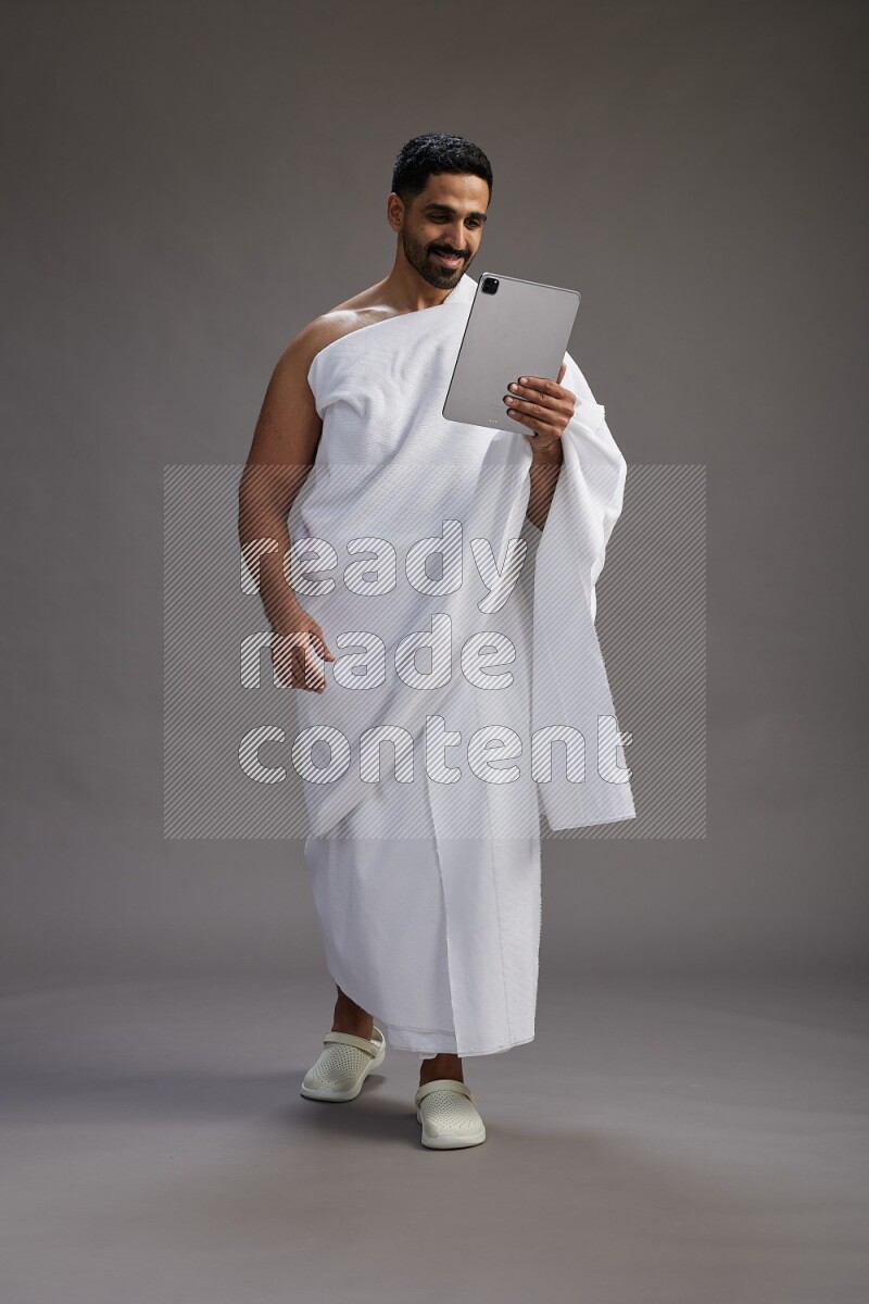 A man wearing Ehram and holding a tablet on gray background