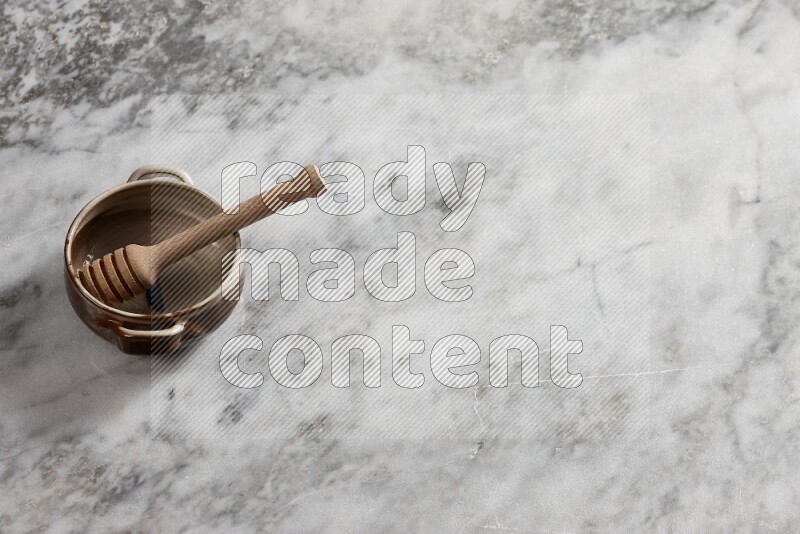 Multicolored pottery bowl with wooden honey dipper in it on grey marble background