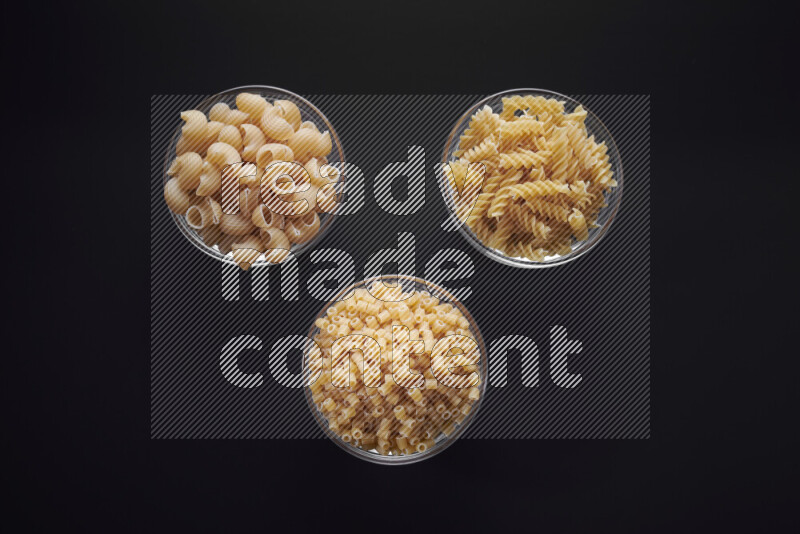 Different pasta types in glass bowls on black background